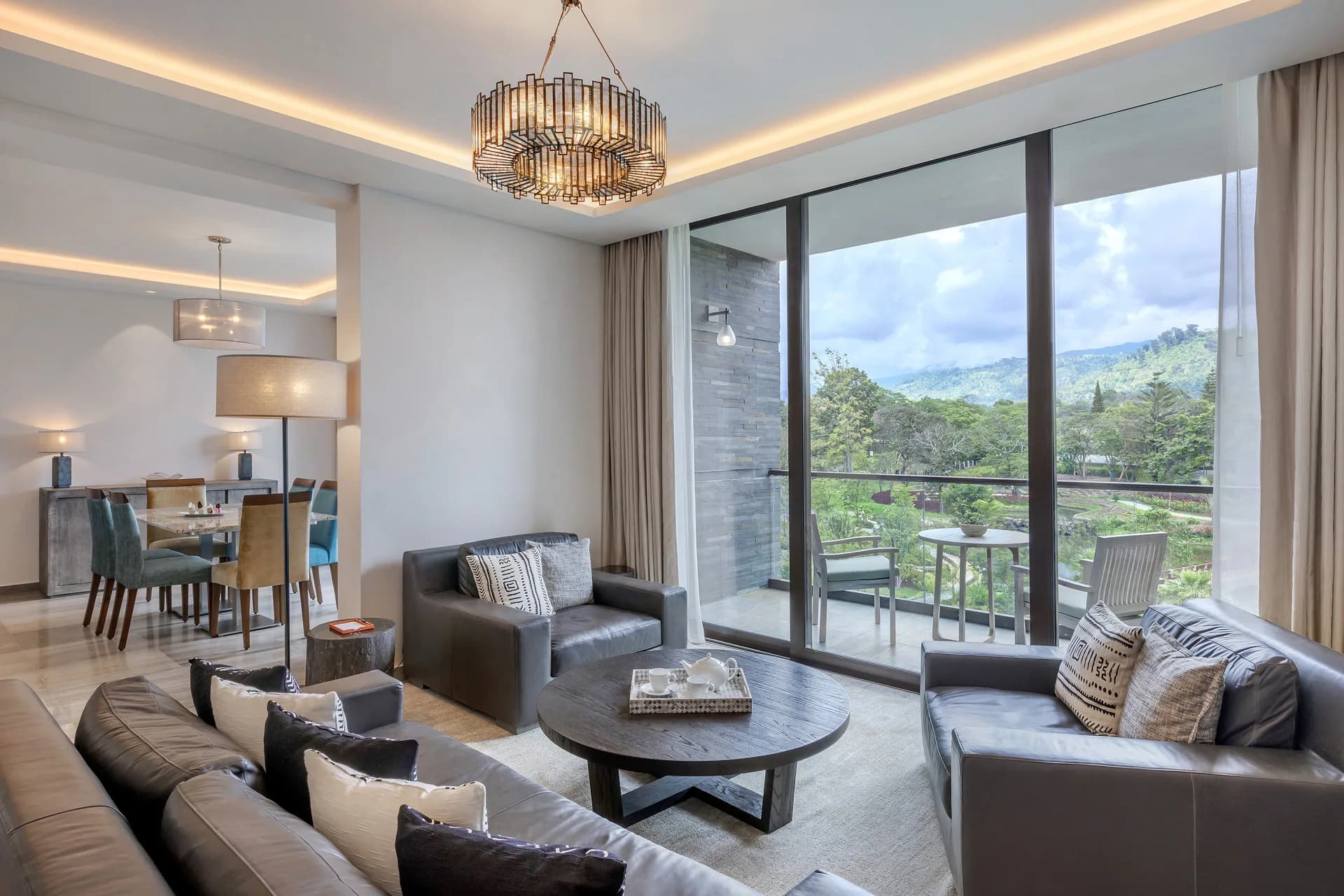Grand Suite living area at Gran Meliá Arusha, with leather sofas, a round coffee table set for tea, and floor-to-ceiling windows facing green hills