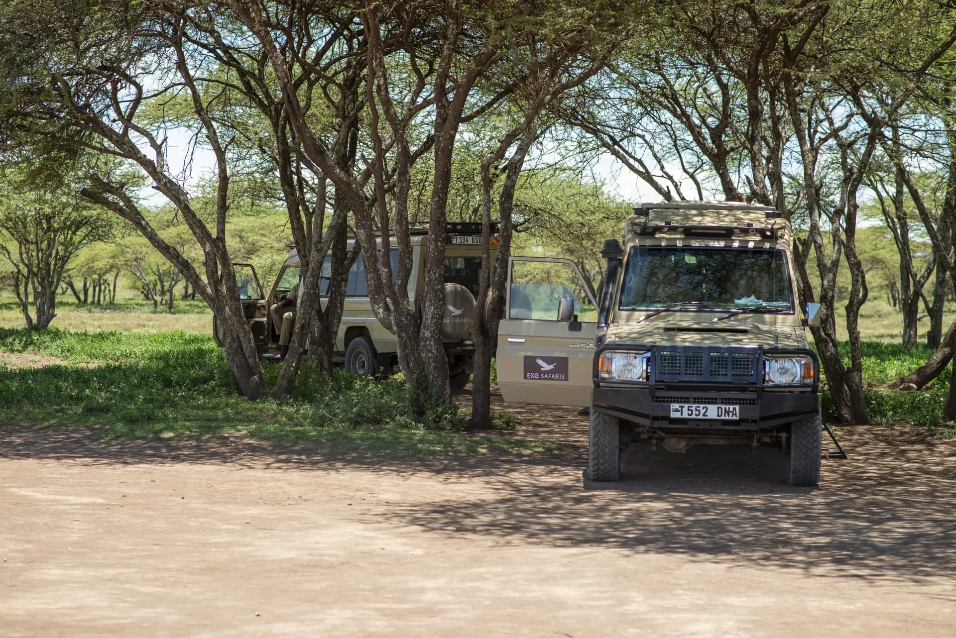 Two EXG Safaris Land Cruisers resting in the shade of acacia trees