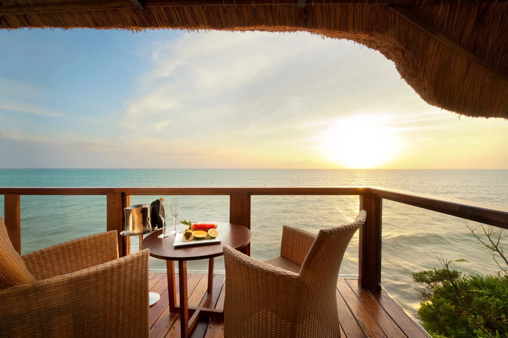 Overwater thatched pavilion set for a private sunset dinner on Zanzibar, with fruit, wine, and champagne overlooking the ocean
